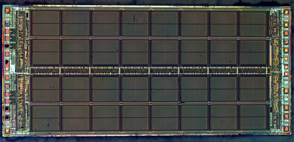 Close-up of a rectangular memory chip die, with a grid of memory cell blocks between rows of contact pads